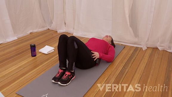 Woman lying on yoga mat doing lumbar rotation stretch.
