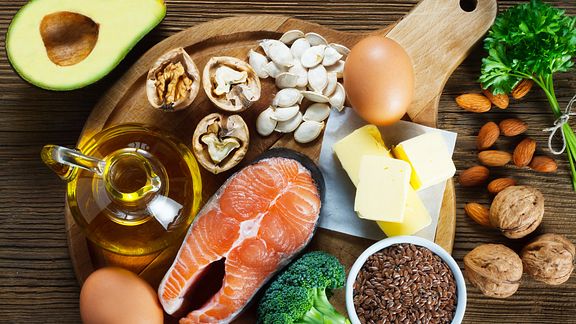 Spread of healthy foods including broccoli, salmon, eggs, olive oil, chia seeds, and avocado