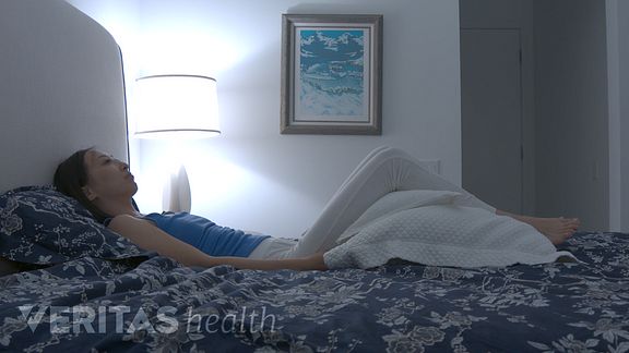 Femme allongée sur le dos sur le lit avec un oreiller sous ses genoux.
