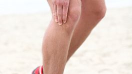 Runner on the beach grabbing knee in pain.