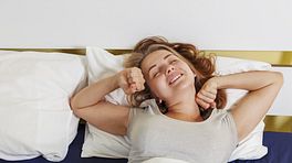 Woman lying in bed, stretching as she wakes up