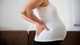Pregnant woman grabbing her lower back in pain.