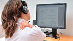 Woman working at a computer, grabbing her neck in pain