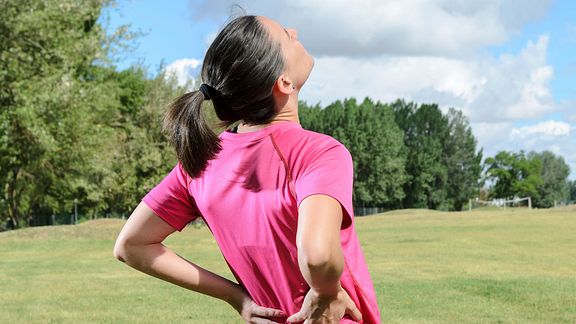 Woman outdoors grabbing her back in pain.