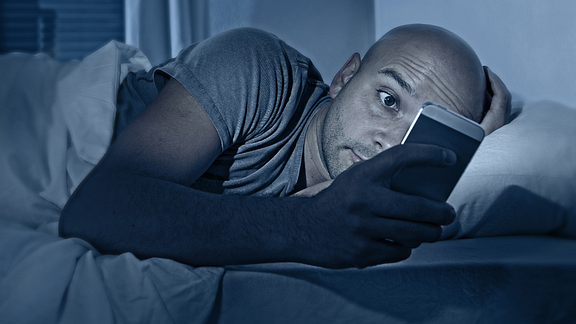 Image of a man checking his cellphone in bed