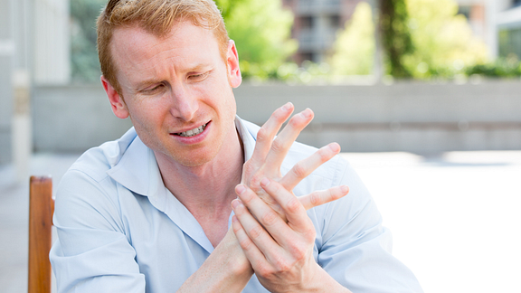 Image of man sitting outdoors holding his had and wrist in pain