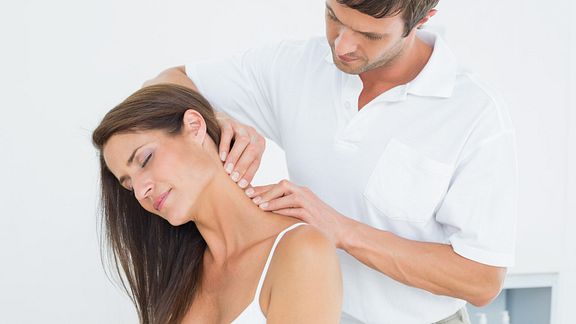 Male physical therapist massaging a young woman's neck in the medical office