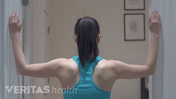 Posterior view of woman doing a corner stretch on a door frame.