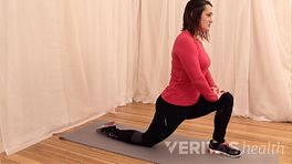 Woman kneeling on her right leg, with her left knee at a 90 degree angle. She's resting her hands on her left knee to stretch the hip flexor muscle.