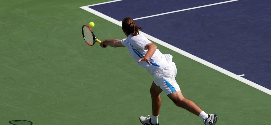 Man playing tennis at USTA Tennis player lunging after a ball with a backhand