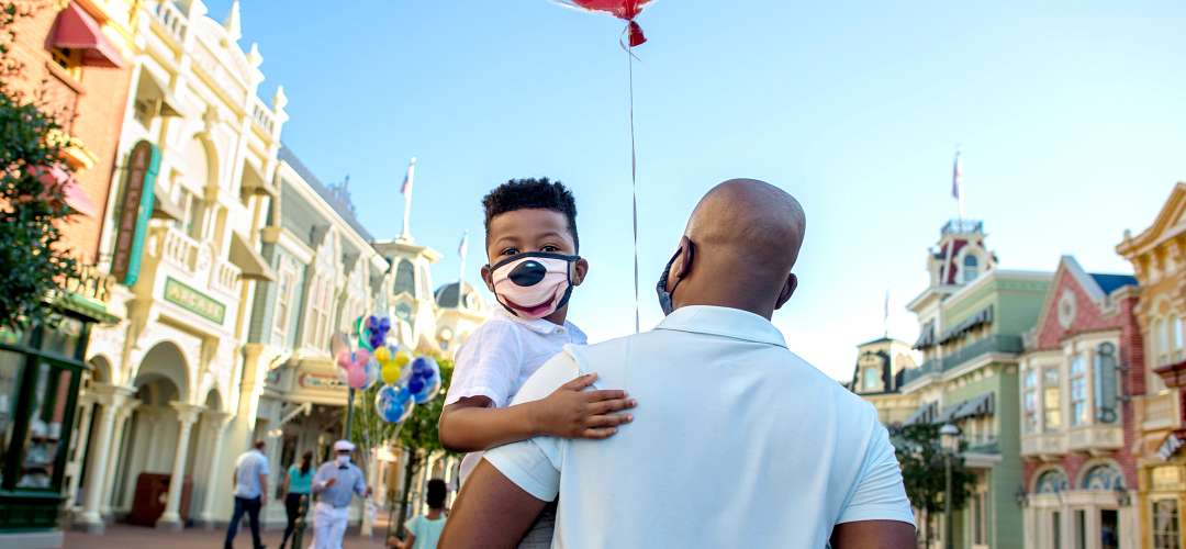 Father and Son at Magic Kingdom A father holding his son while walking in the Magic Kingdom. Both are wearing face masks.