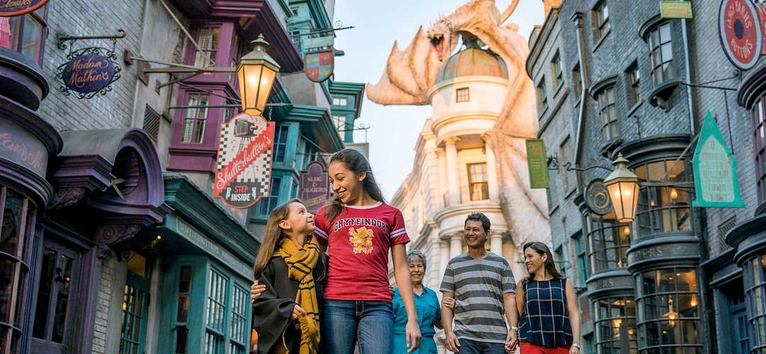 Wizarding World of Harry Potter, Diagon Alley Two young ladies walking in front of their parents and grandmother in Diagon Alley with a dragon perched on top of a building in the background.