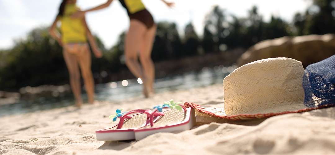 Wind-away River at Discovery Cove Sandals and a hat on the sand in the foreground, while a mother and daughter head back to the river in the background.
