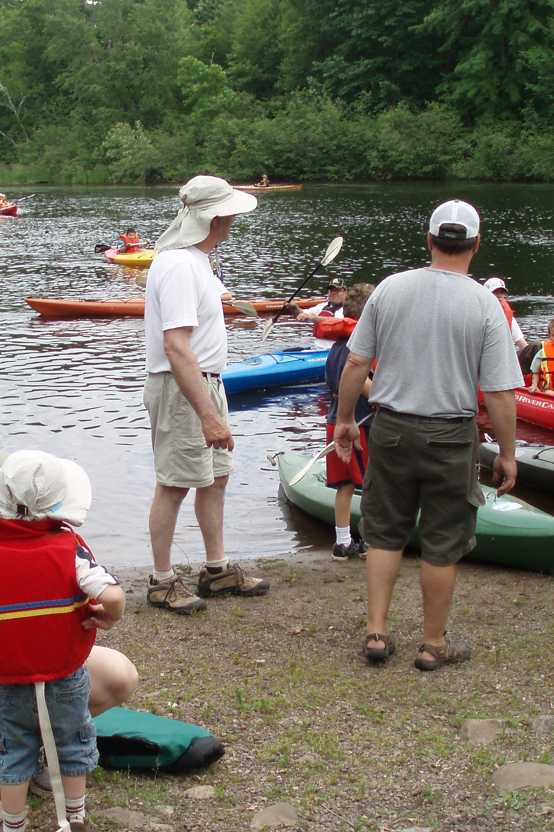 Men helping young children in kayaks on shore of lake