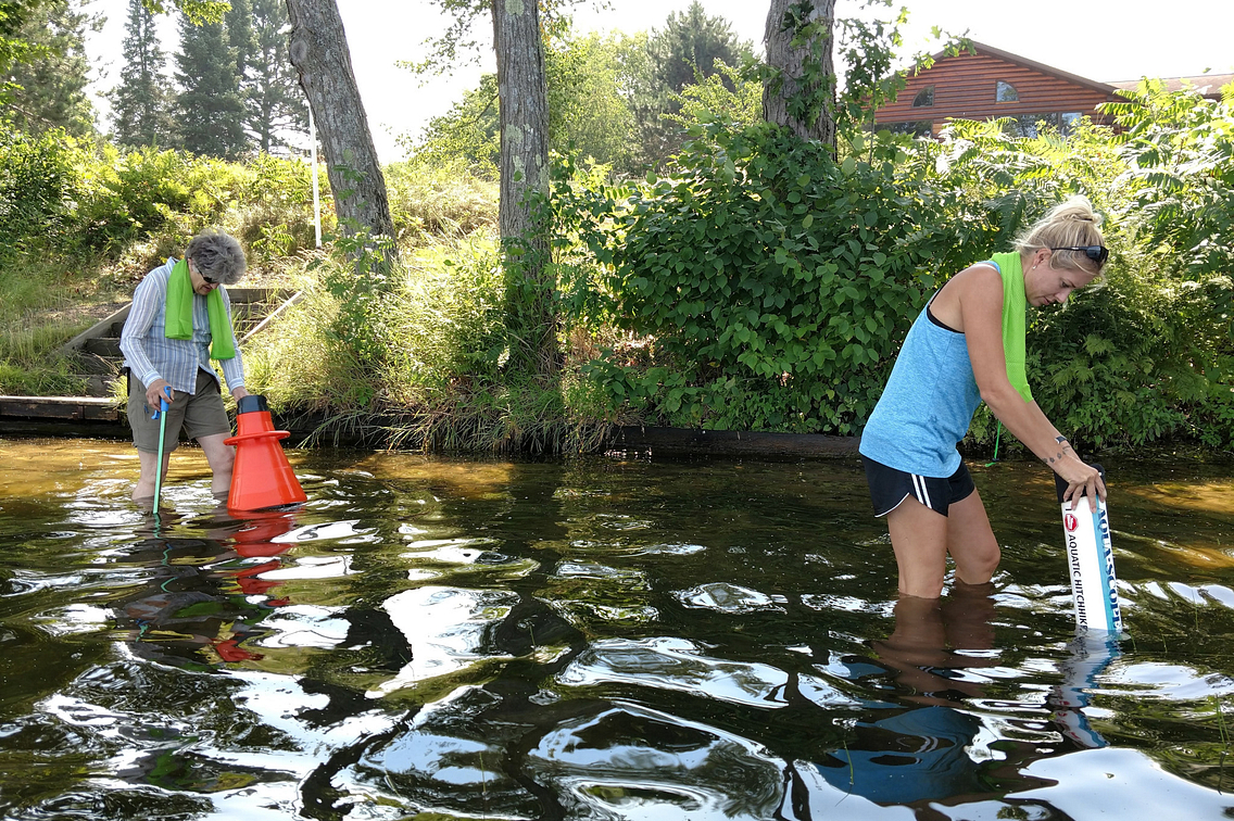 Two women wading in water to their knees using apparatus to see underwater