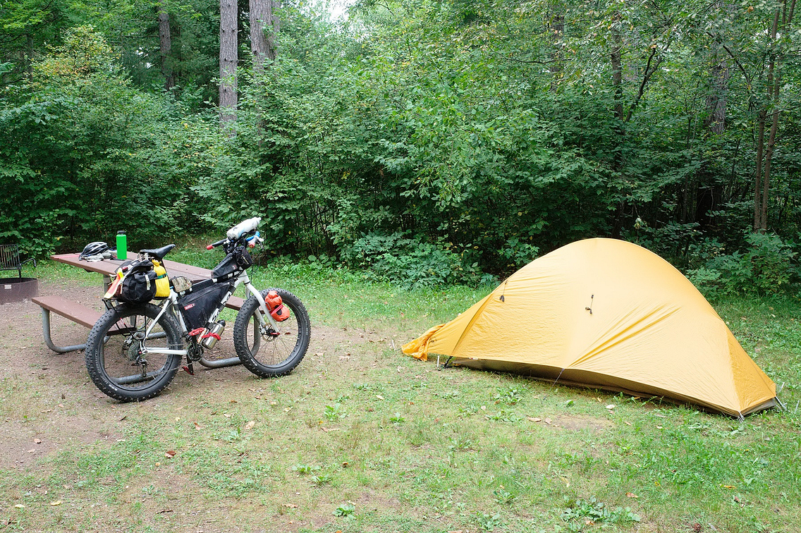A fat-tire bike rests against a picnic table with a yellow tent set up nearby
