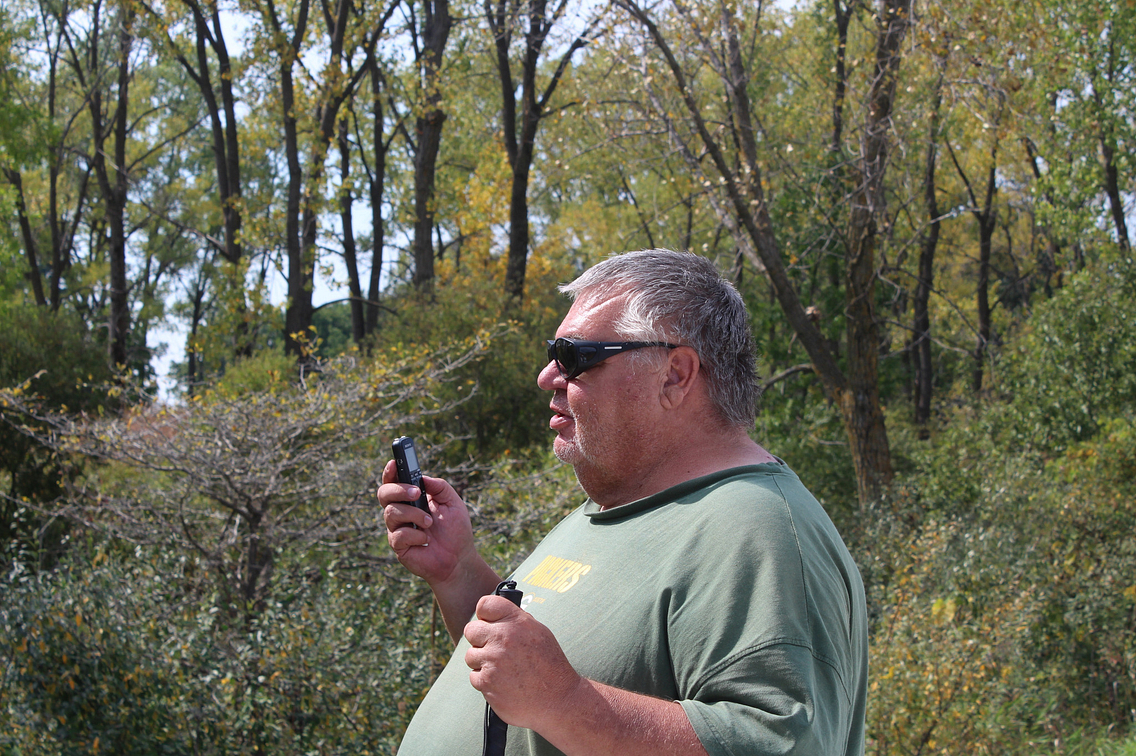 Man in forest with sunglasses on, holding a cell phone