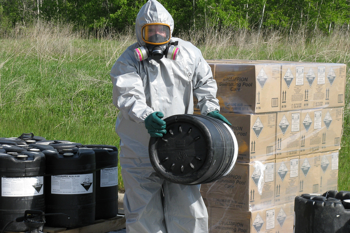 Man in haz-mat suit transferring barrels of hazardous material