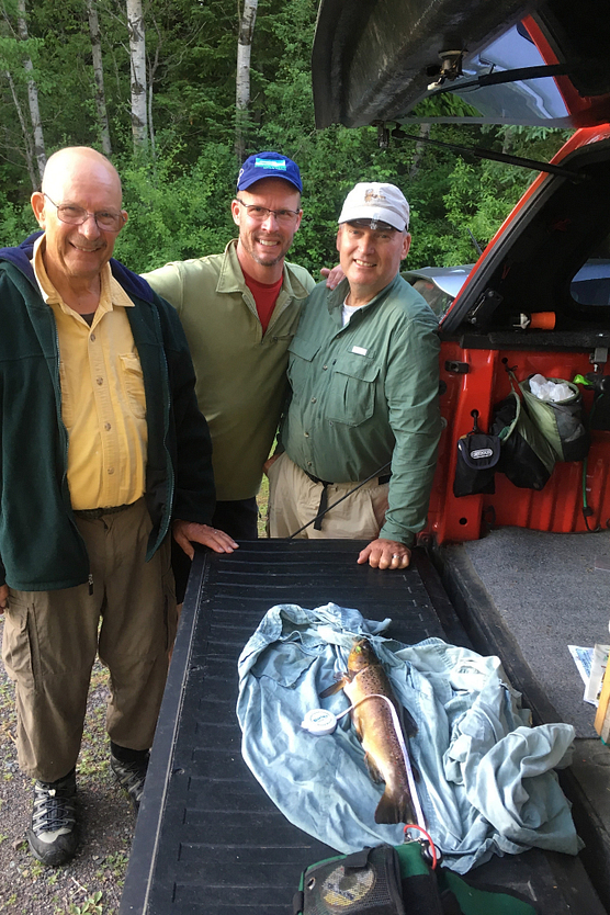 Three fishermen standing at back of pickup looking at large trout
