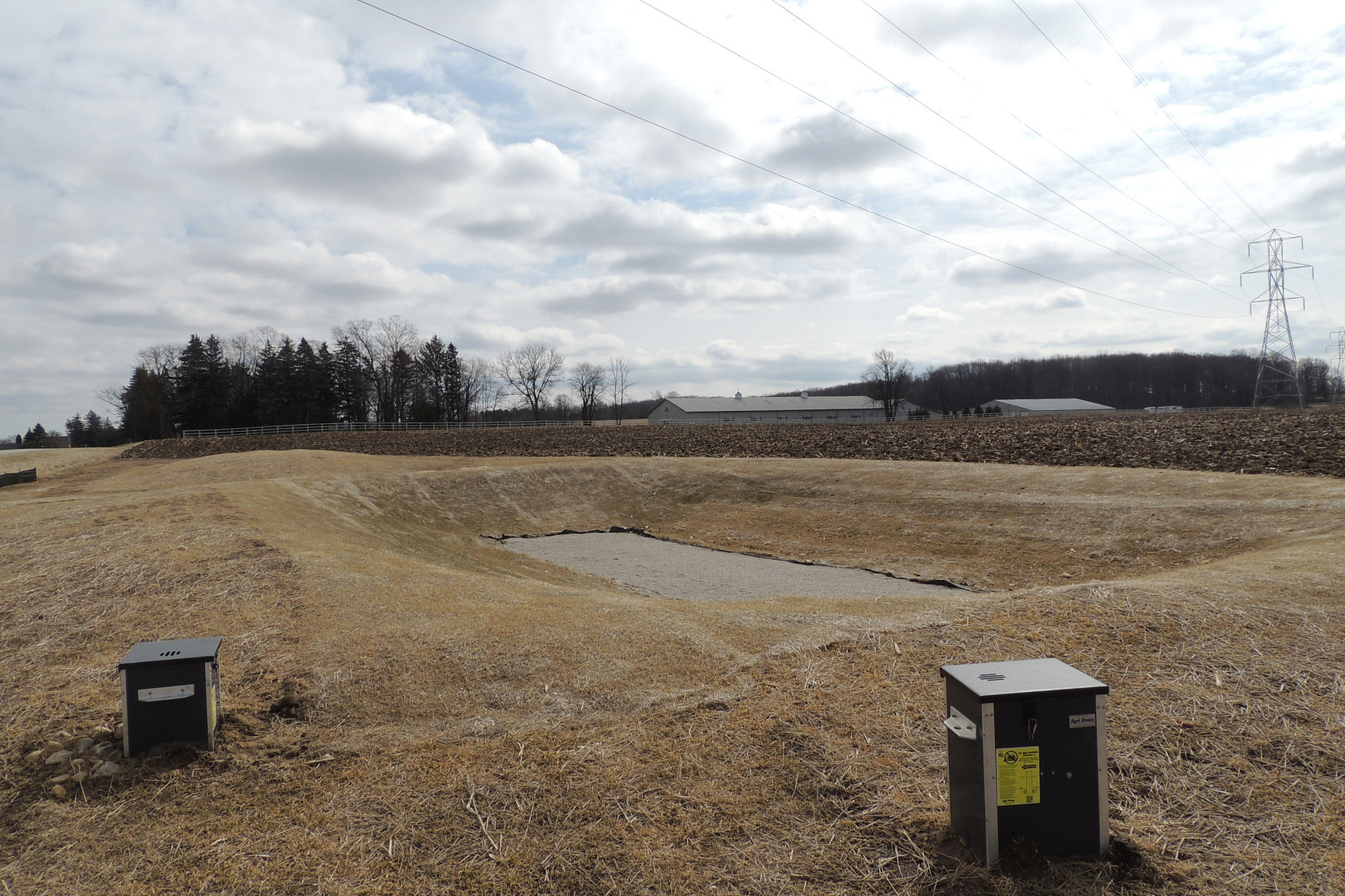 Excavated depression in agricultural setting with two box-like pieces of equipment