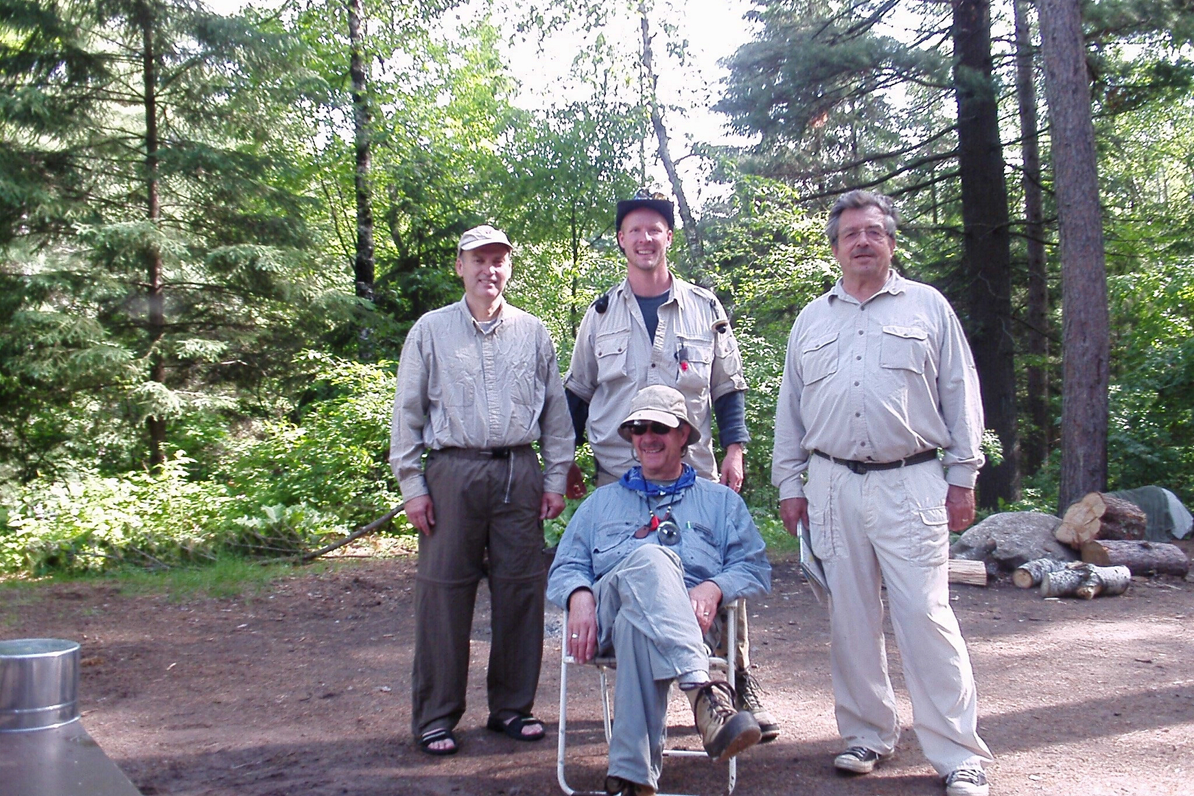 Four men in fishing clothes, three standing and one sitting