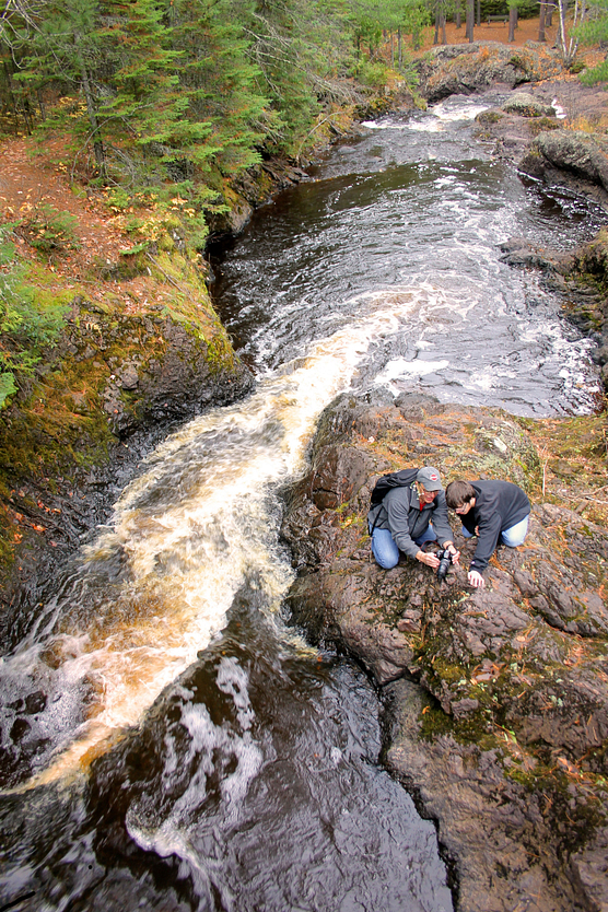 Photo of two people taking a photograph on rock overlooking fast-moving river