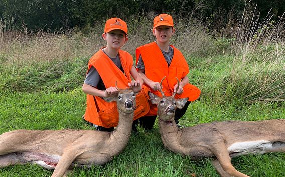 two boys in orange hunting vests with harvested deer