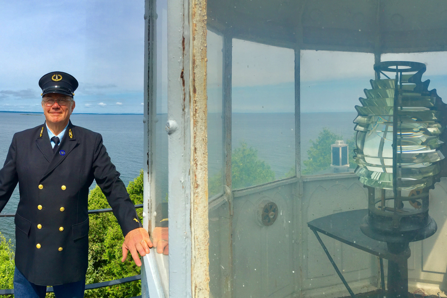 Man in naval-type uniform with visored cap standing on lighthouse stairway with blue water and sky in background