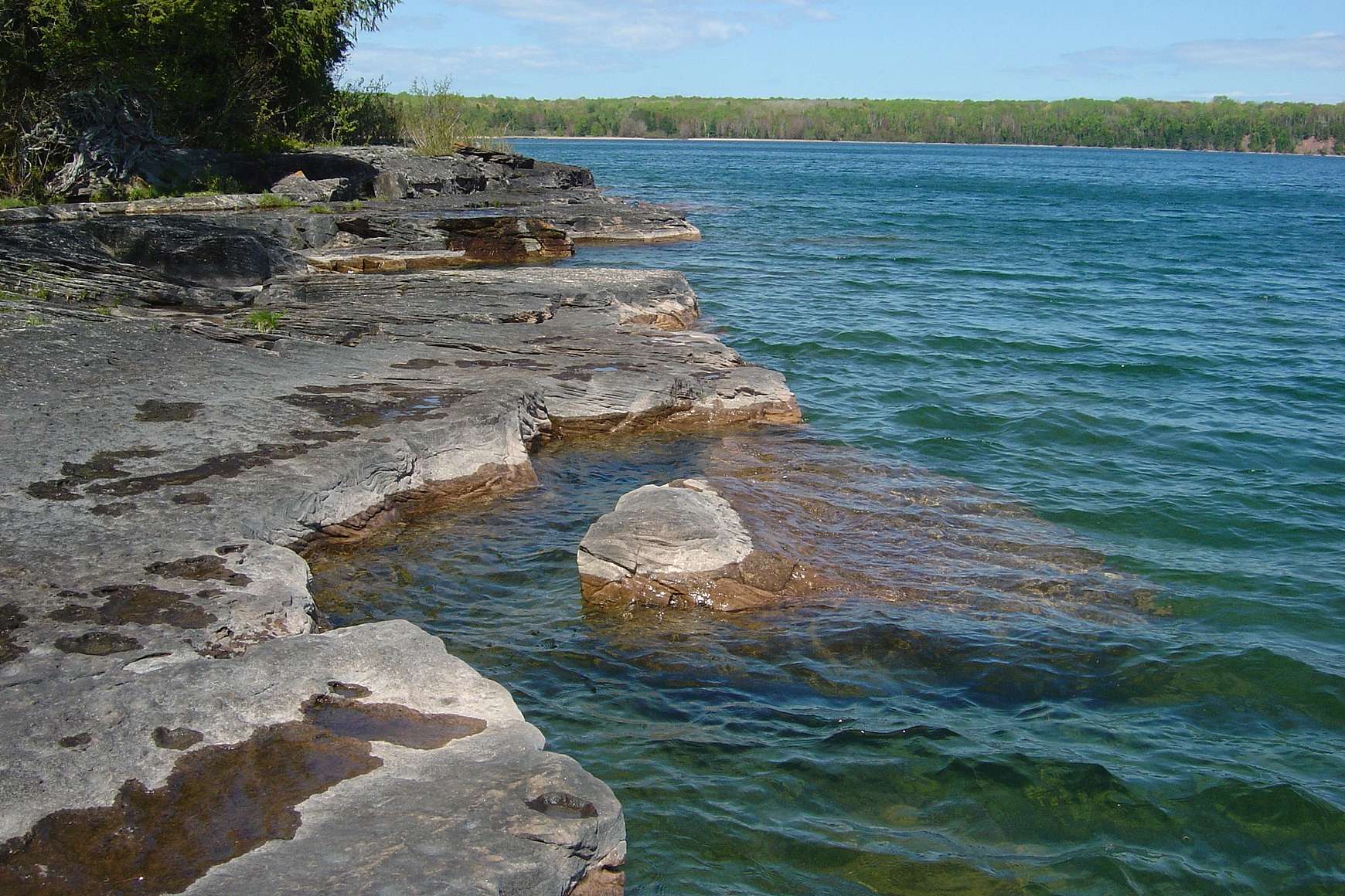 Rocky shoreline of Lake Superior on Stockton Island with blue water, trees and blue sky