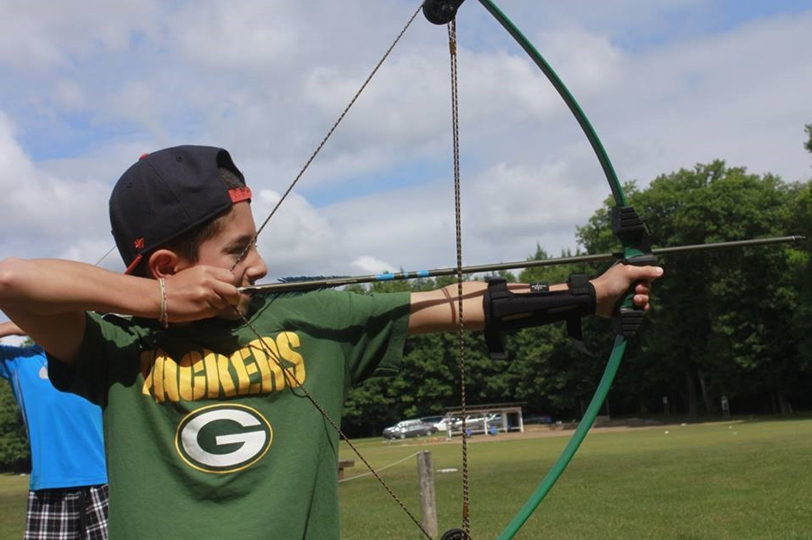 Young boy in green shirt participating in archery lesson