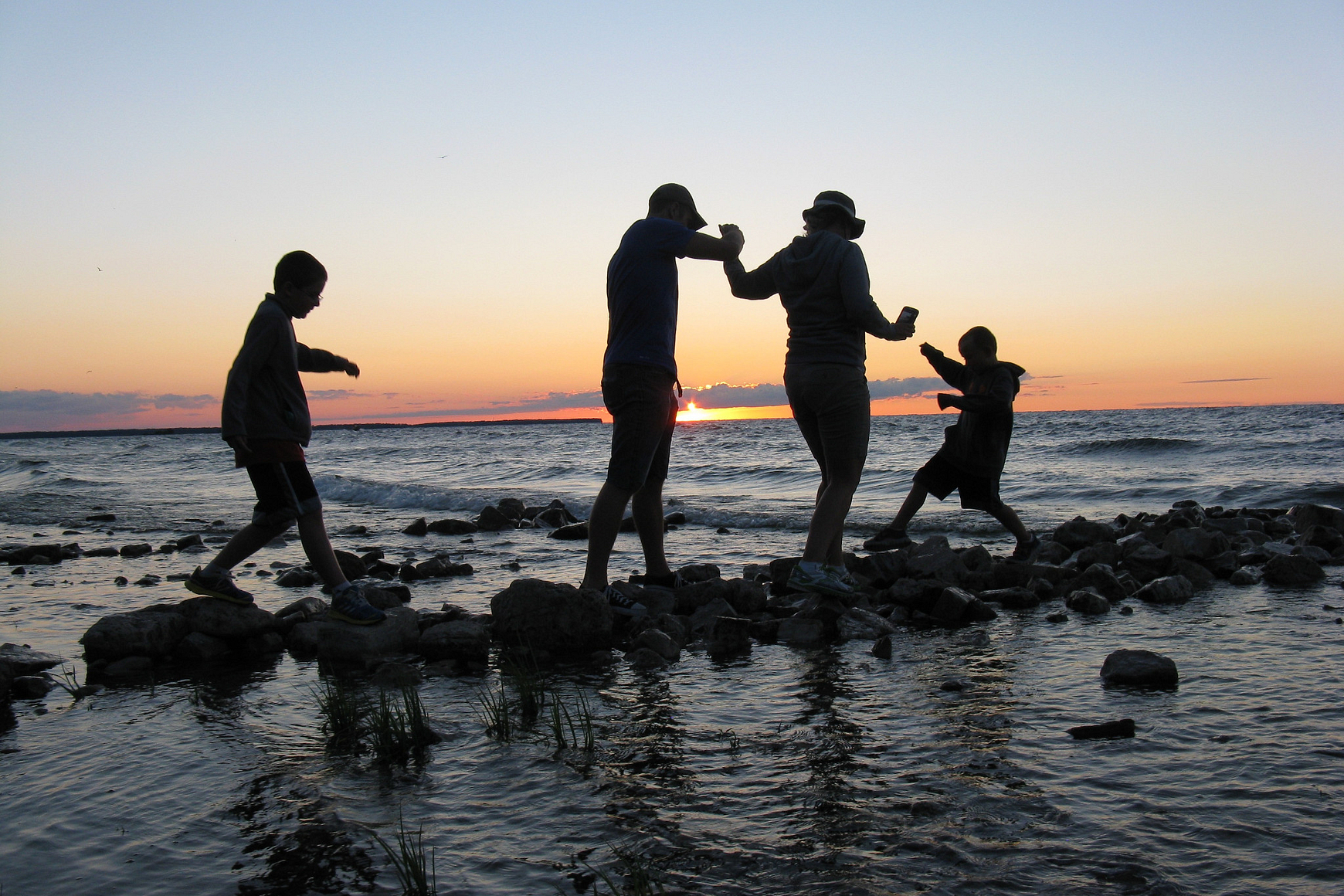 Family walking across stones near shore of Lake Michigan, silhouetted against sunset