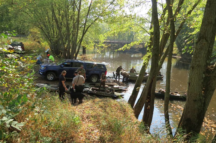 people examine boats for invasive species near marshy waterway