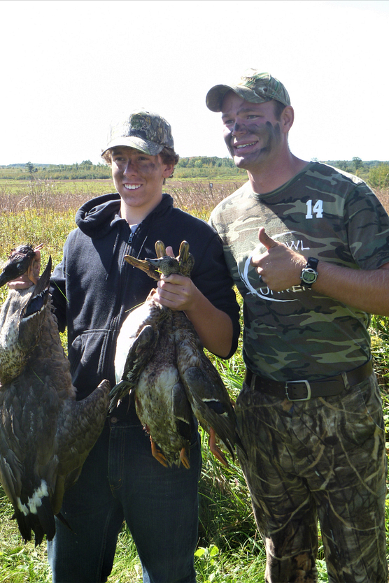 Young man holding two handfuls of waterfowl with an older man standing next to him giving a thumbs-up