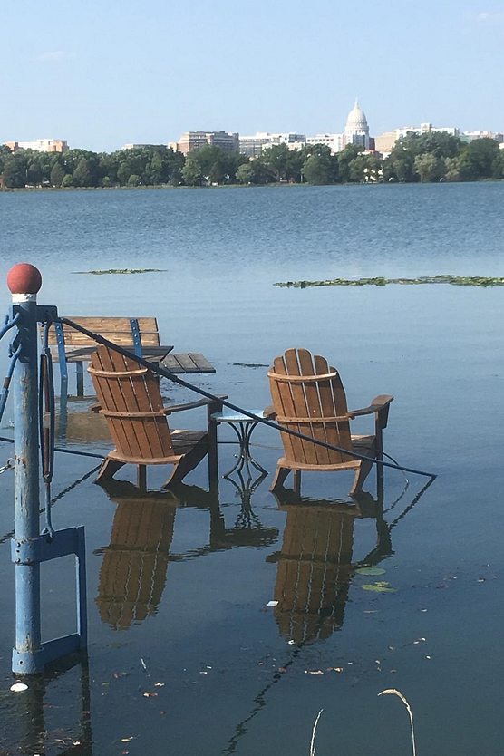 Photo of lawn chairs in flooded yard on shore of Lake Monona with capitol in background