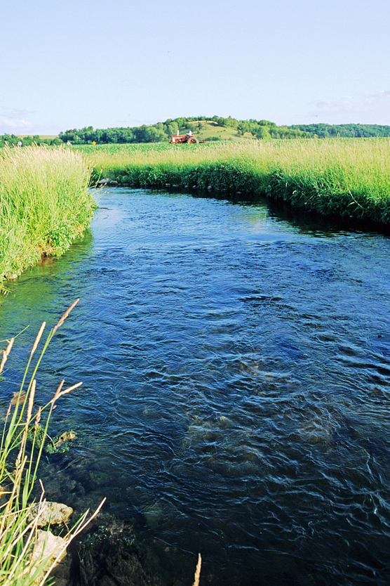 Clear blue stream with farm scene and tractor in the distance