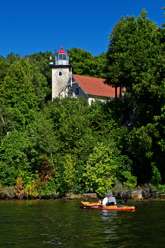 Man in kayak looking up at the Eagle Bluff Lighthouse