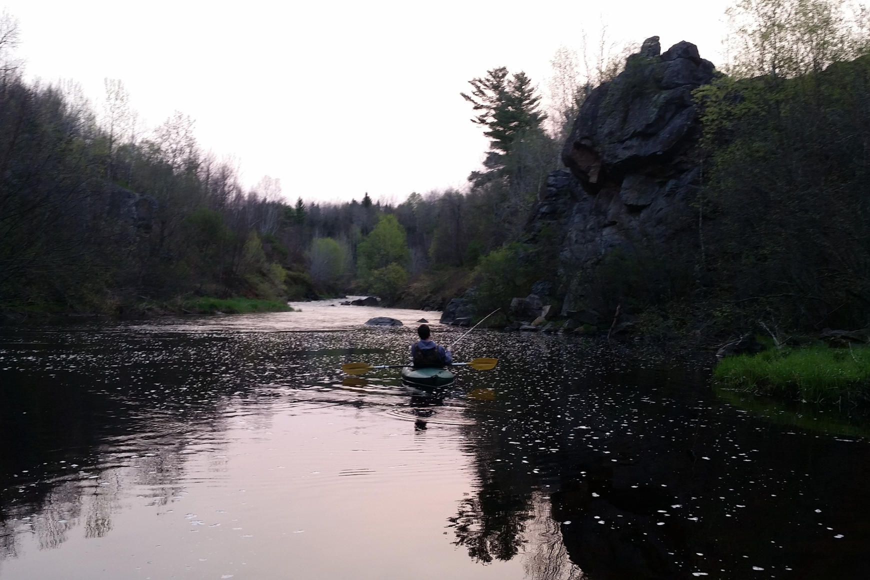 Photo of a kayaker fishing in a serene river setting