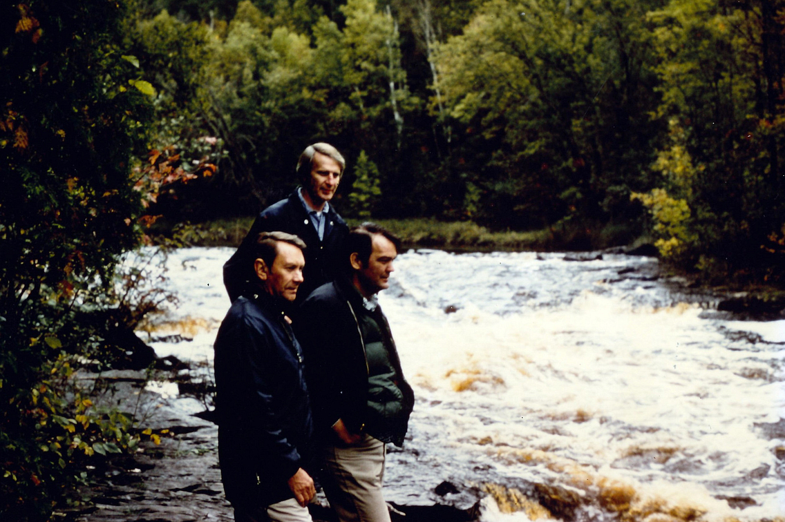 Three men standing near a waterfall