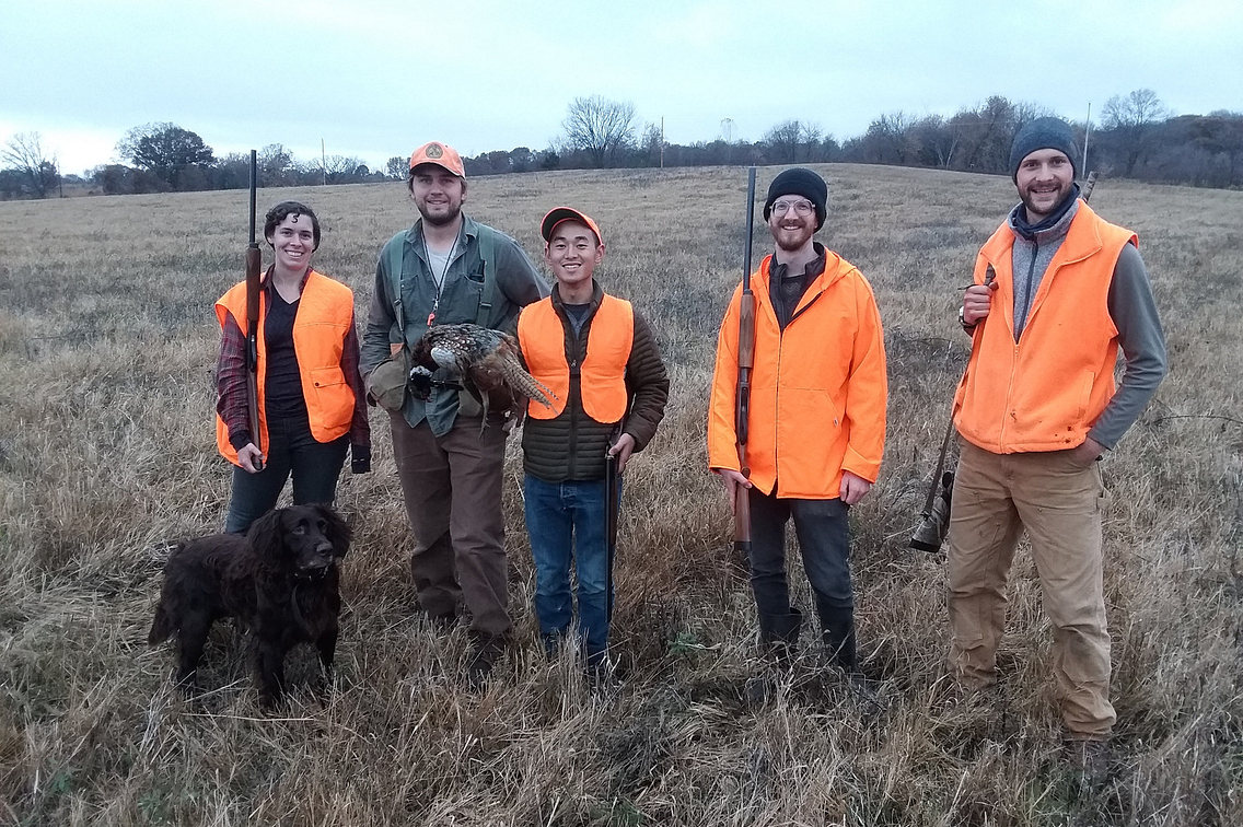 Group of hunters standing in field, with a dog.