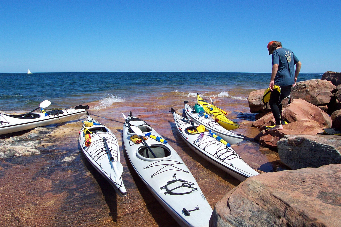 Sea kayaks are lined up on shore of Lake Superior with blue sky and blue water