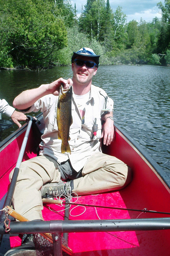 Man in a canoe with a big smile, holding trout he caught