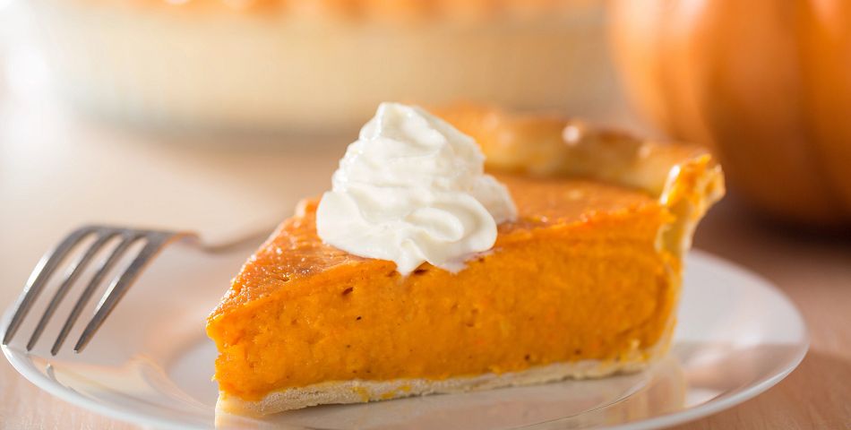 Pumpkin pie with whipped cream dollup on white plate with fork
