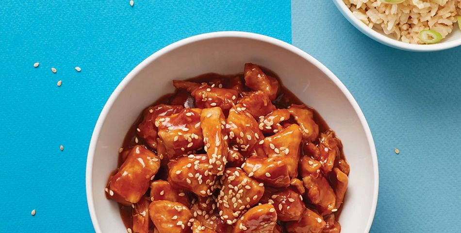 Sesame Chicken in bowl on table with chopstickets and bowl of rice