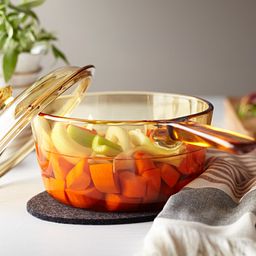 Visions 4-piece Cookware set with stew inside stewpot, macroni in inside saucepan sitting on the counter on a cutting board